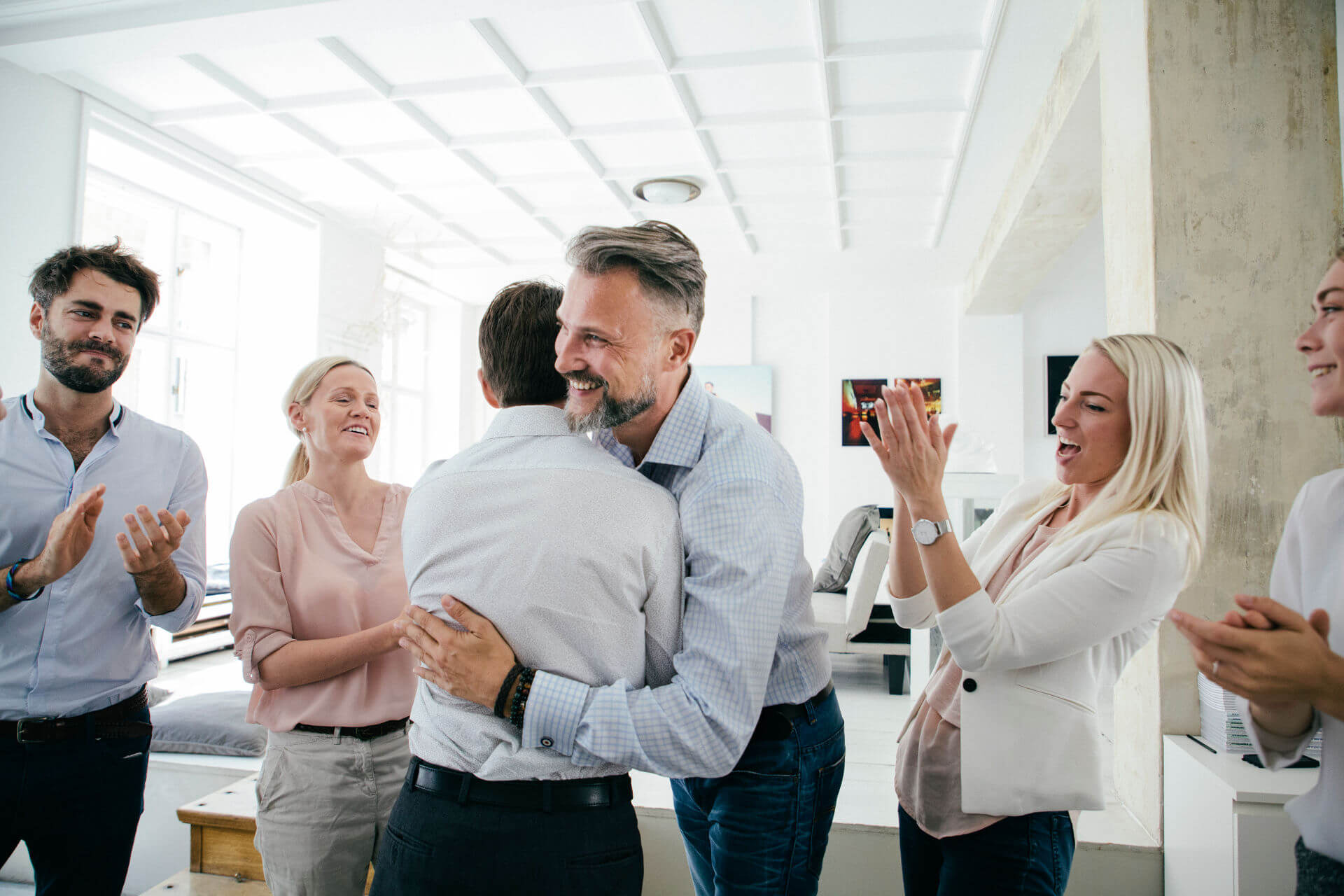 men hugging in an office while people clap